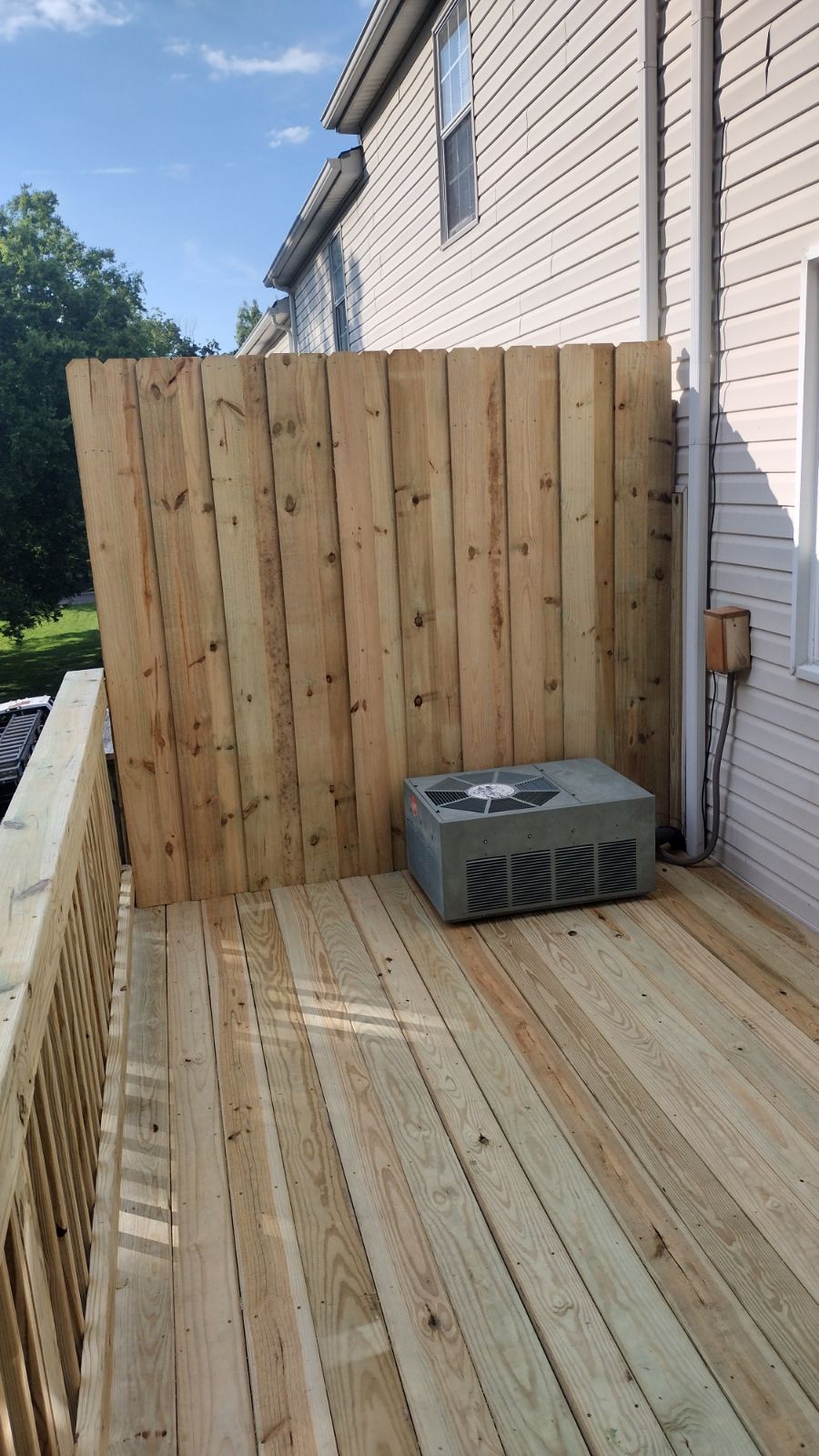 Wooden deck beside a house with a privacy fence and an outdoor air conditioner unit.