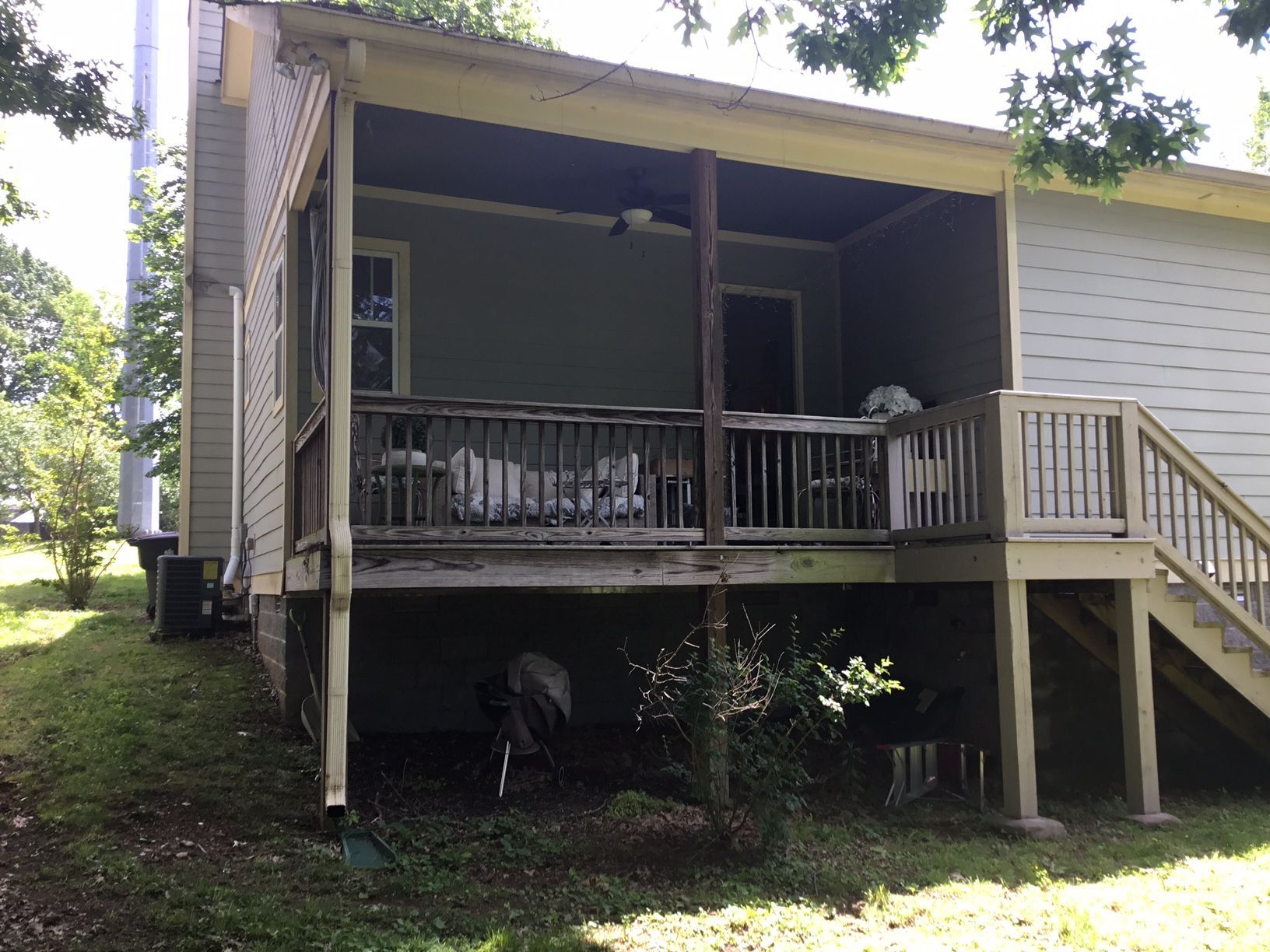Covered wooden porch on a house with stairs, railing, and shaded yard beneath.