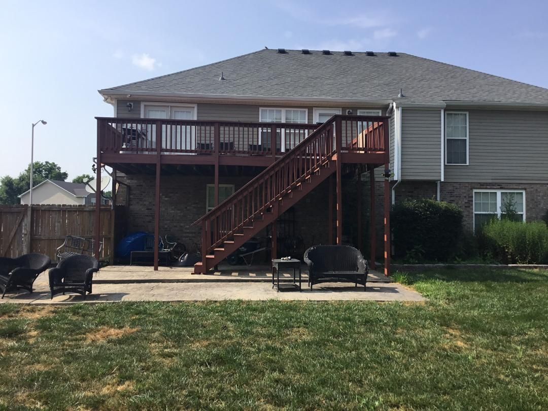 Backyard deck with central stairs, black chairs, and a grassy yard beside a house