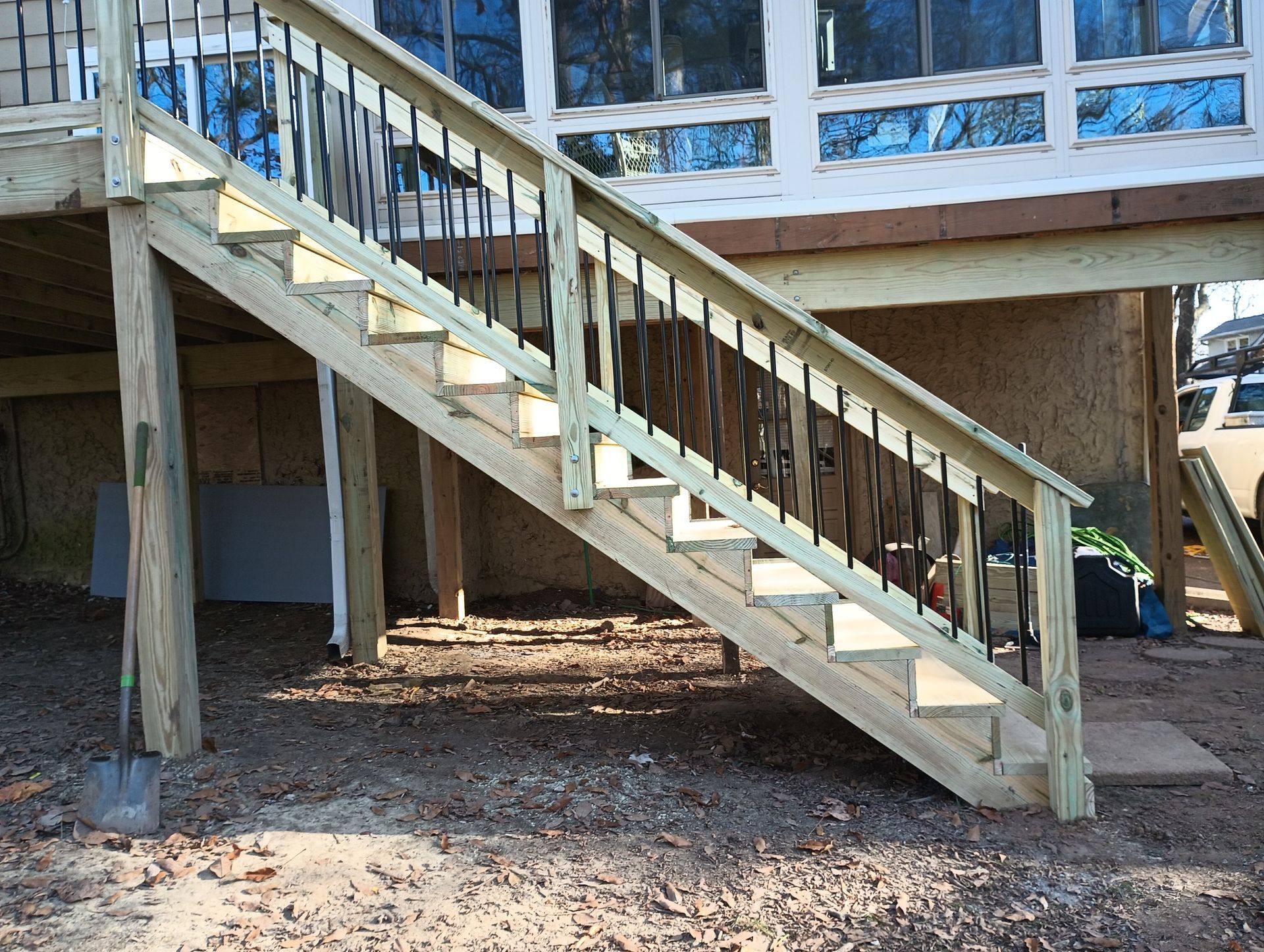 Wooden outdoor staircase leading to a raised porch on a house, with railings and dirt ground below