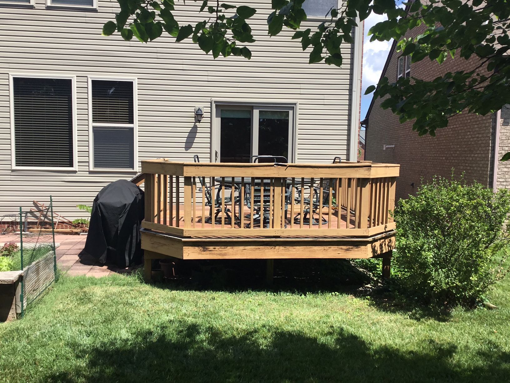 Backyard wooden deck behind a house, with a covered grill and patio chairs.