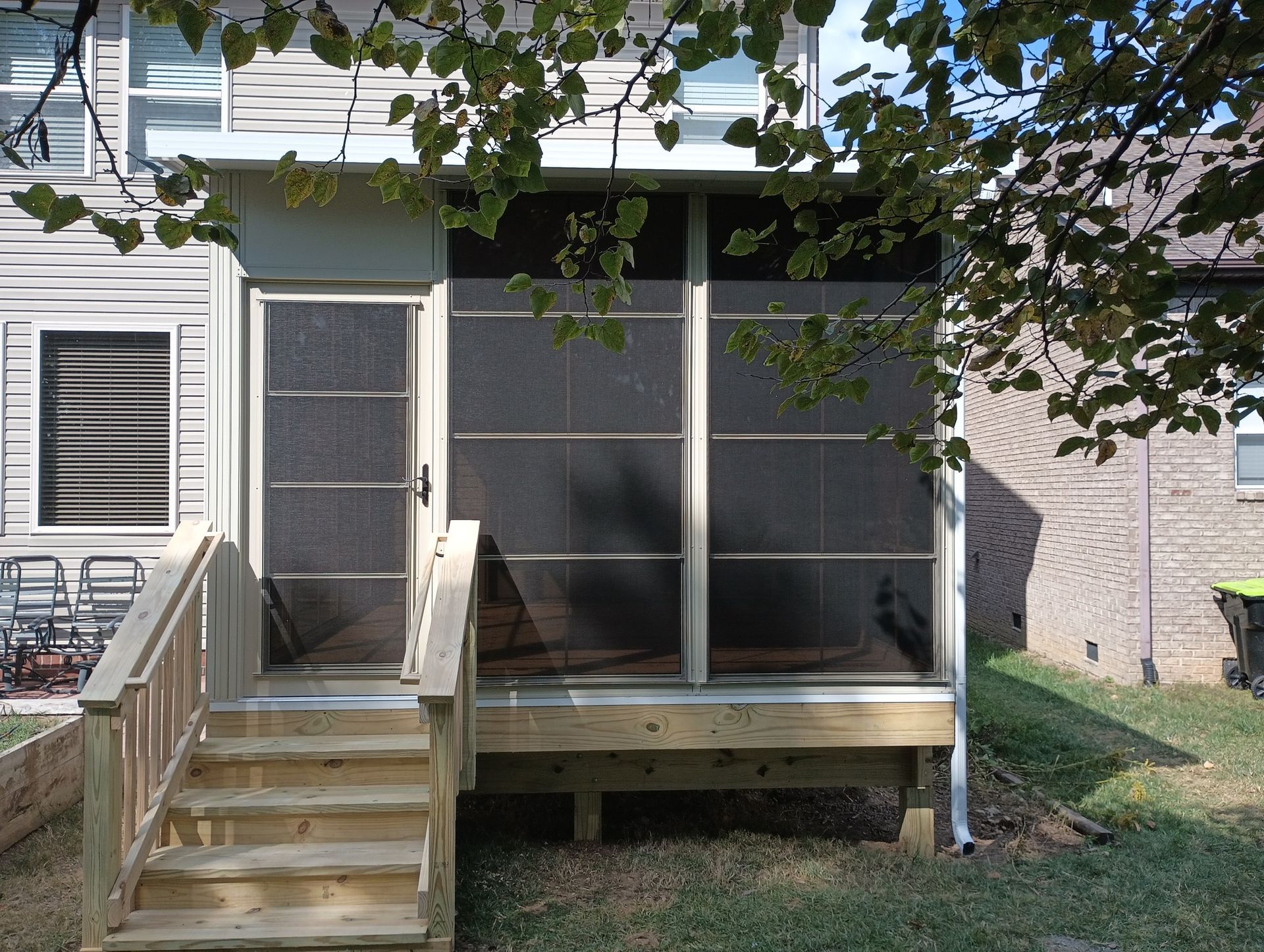 Small front porch with wooden steps, screened enclosure, and a door on the left, shaded by tree branches.