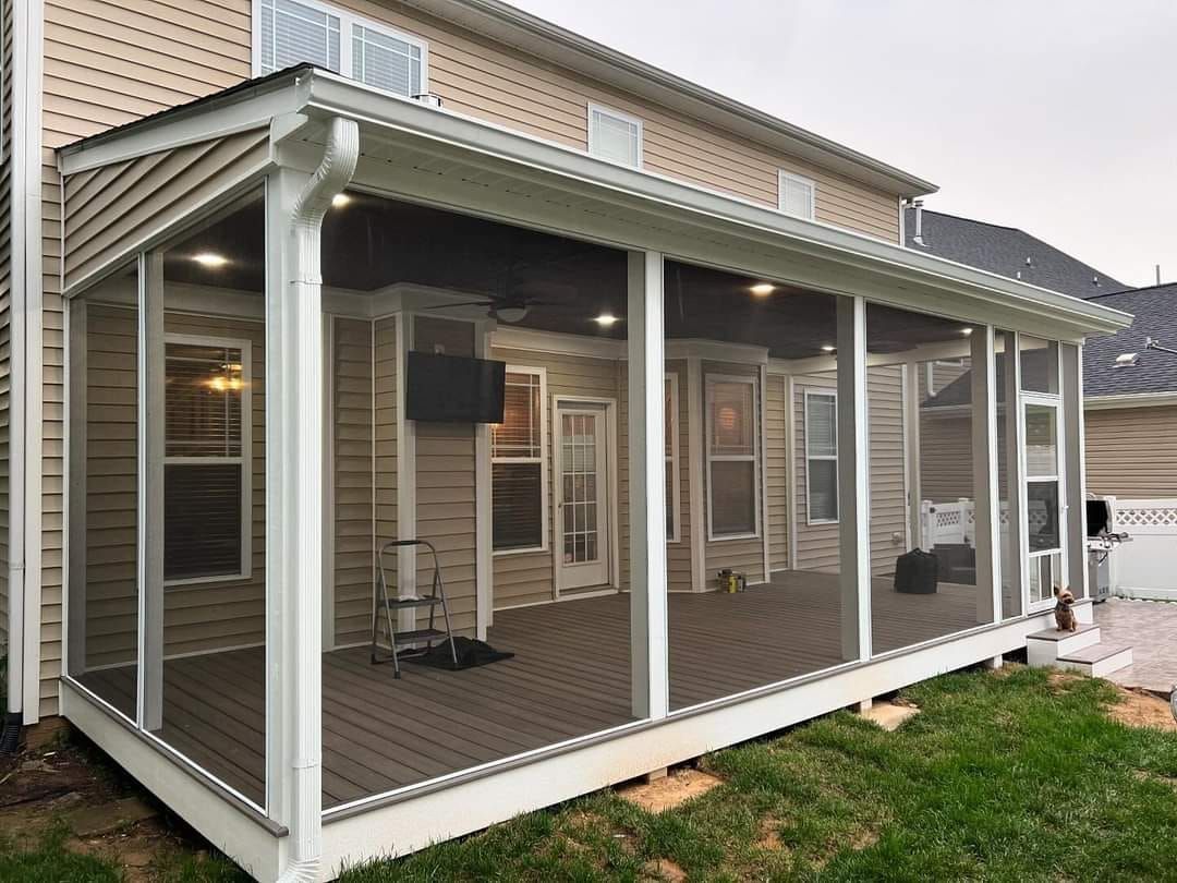 Covered porch with white posts, screen panels, and wood deck attached to a beige house.
