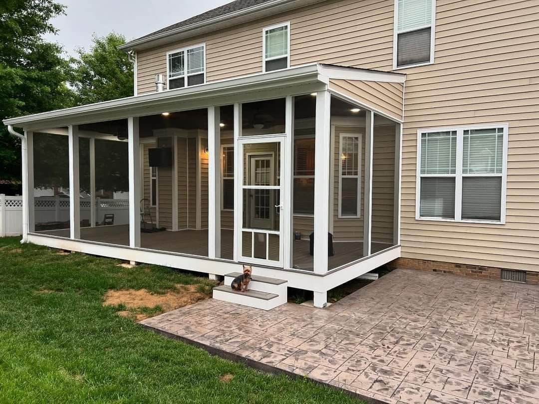 Covered backyard patio with white posts and screened porch attached to a beige brick house.
