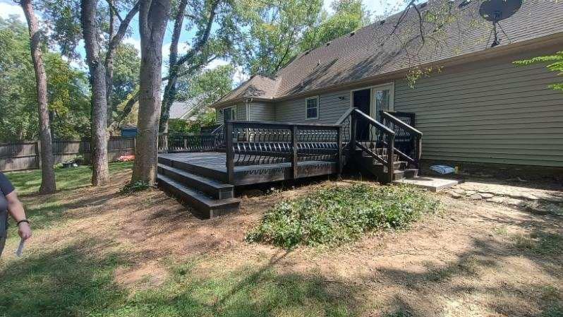 Wooden deck with steps beside a beige house, surrounded by trees and dry ground.