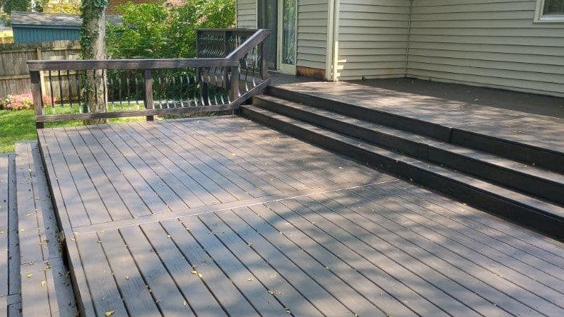 Wooden deck beside a house, with steps leading to a railing and a grassy yard.
