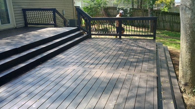 Wooden deck with stairs and railings, with a person standing near the fence in the background.