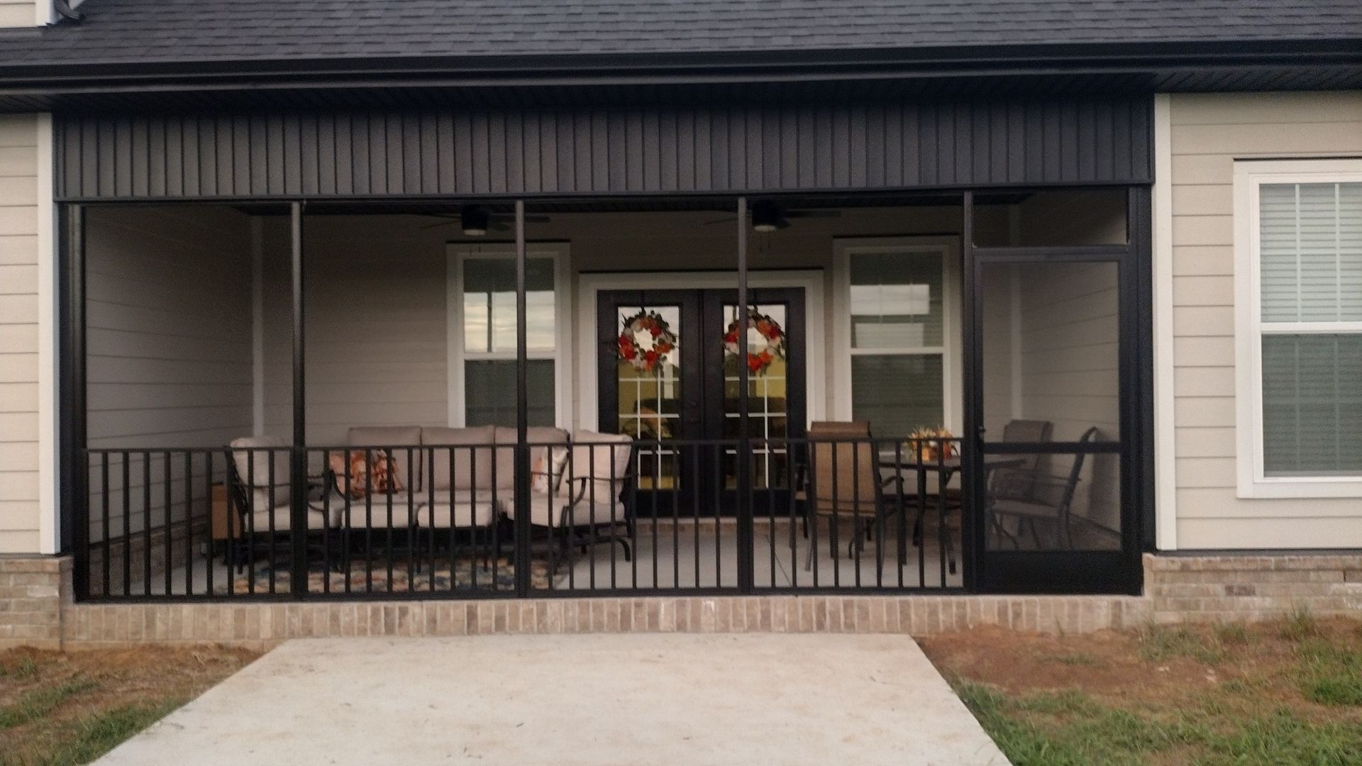 Covered front porch with black railing, outdoor seating, and a sliding glass door on a house facade.