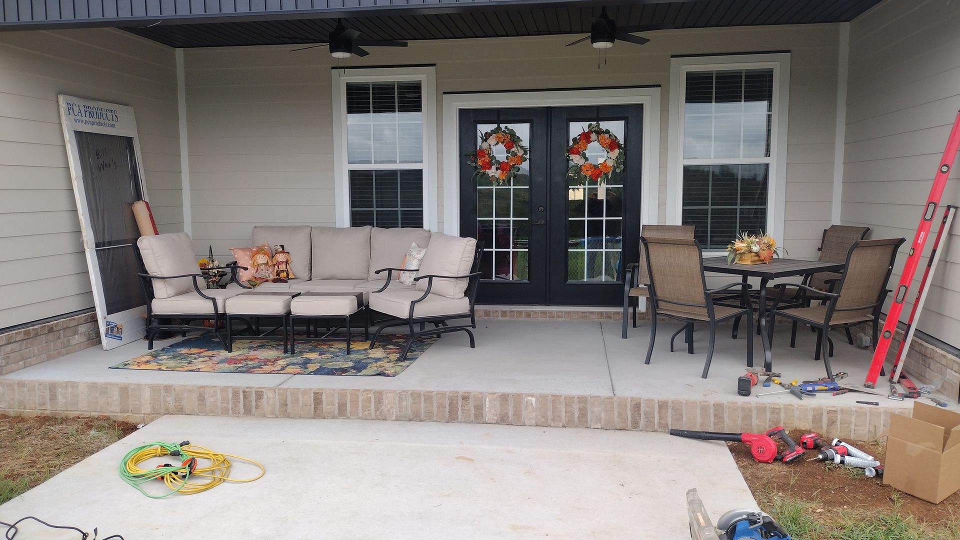 Front porch with patio furniture, black double doors, and holiday wreaths, under a covered roof.