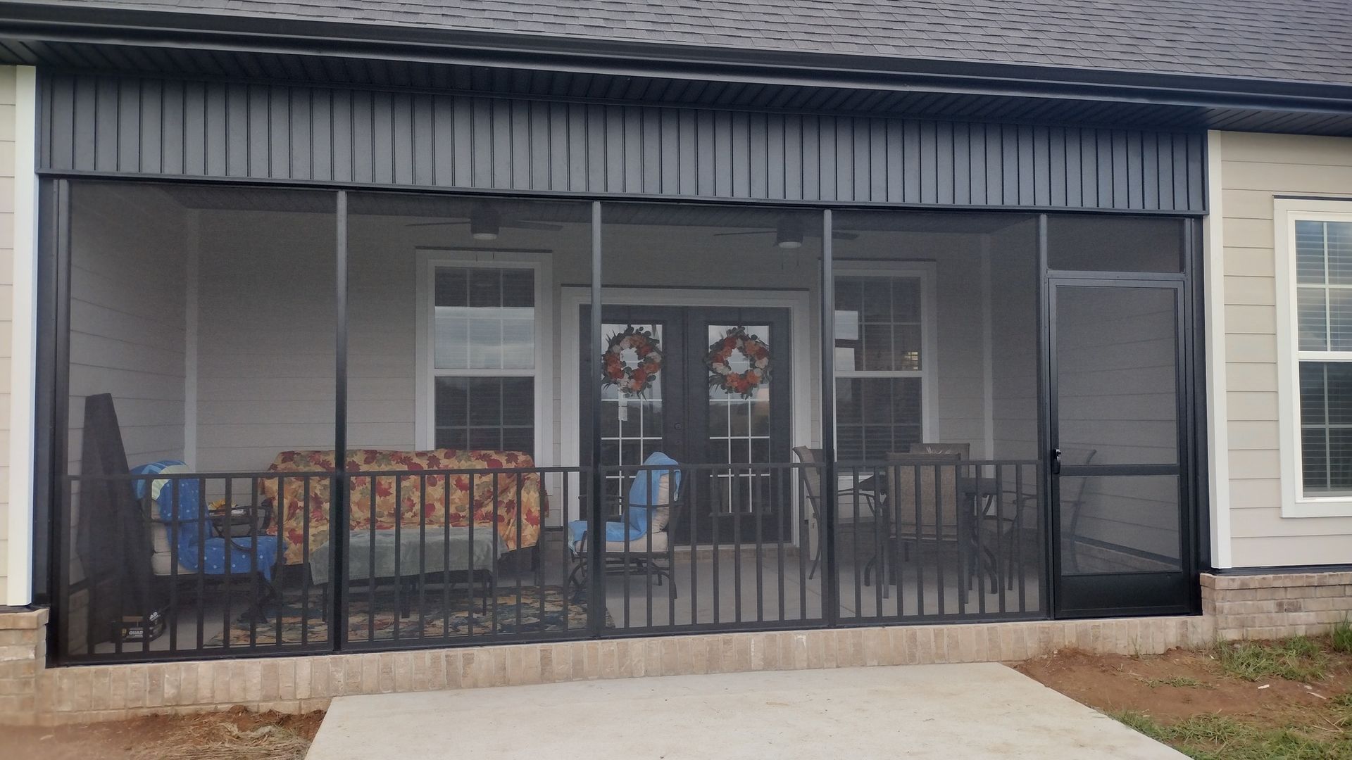 Front porch of a house with black railing, glass doors, and a bench under the covered entry.