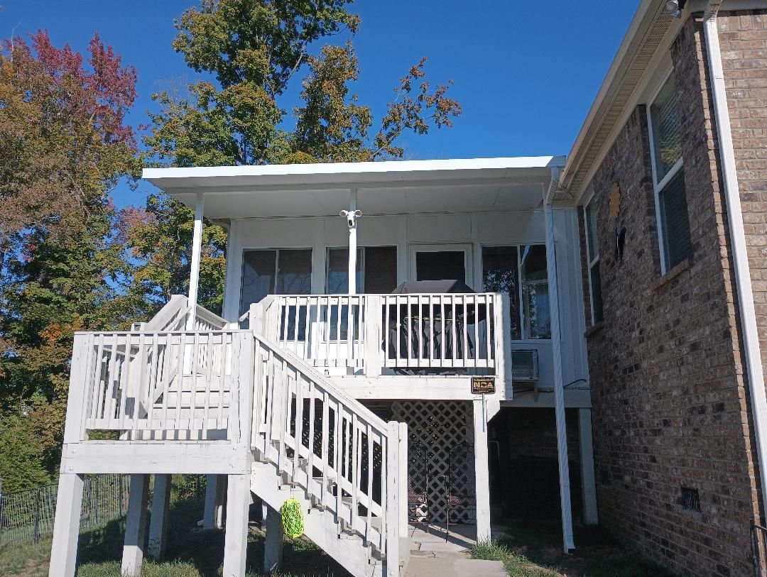 House exterior with white stairs, porch, and railing beside a brick wall under a blue sky