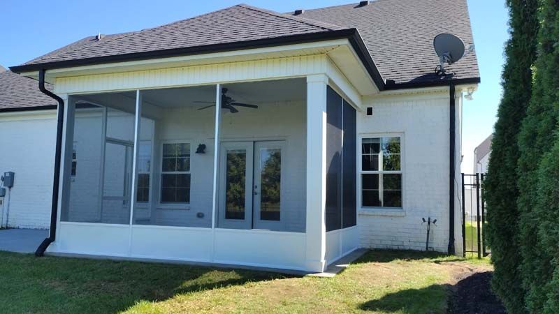 White house with screened porch, dark roof, and a small satellite dish in a sunny backyard.
