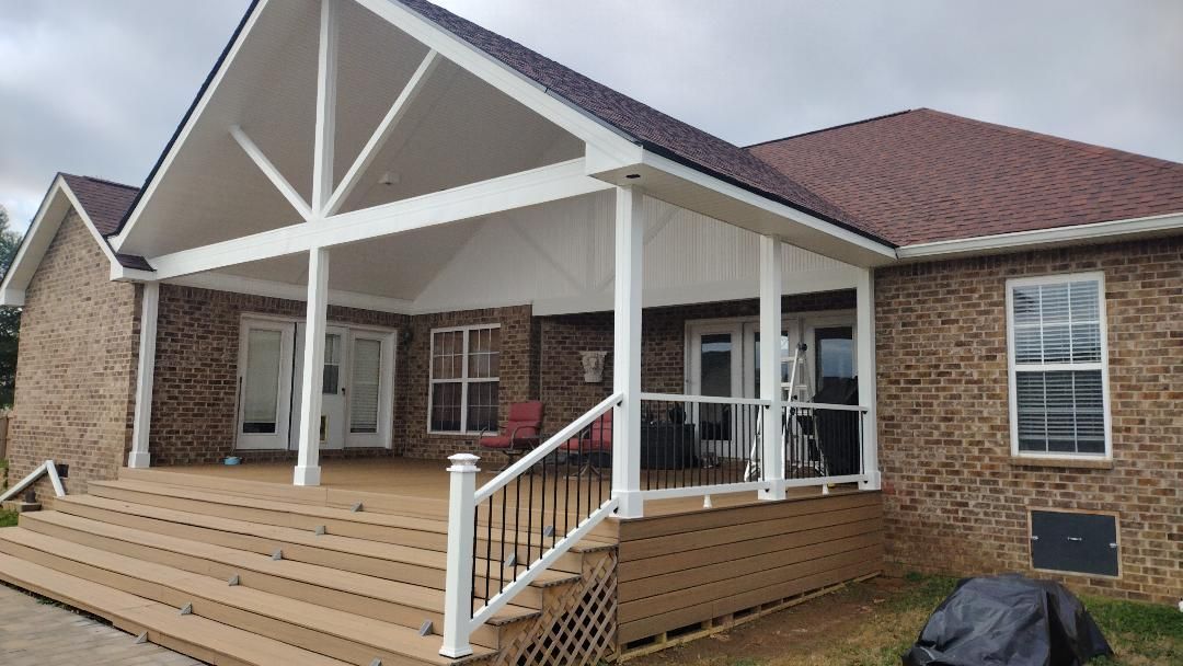 Brick house porch with white columns, wooden deck steps, and a red roof under cloudy skies
