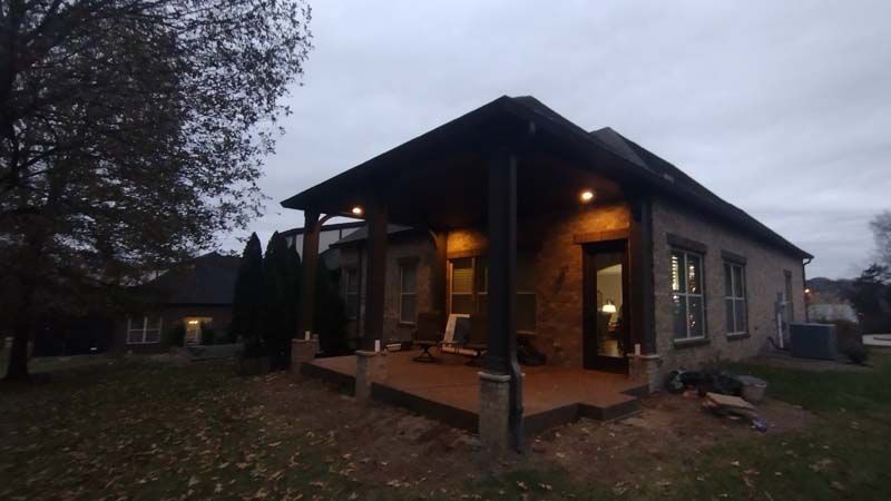 Warmly lit brick house porch at dusk with outdoor seating and trees in the yard