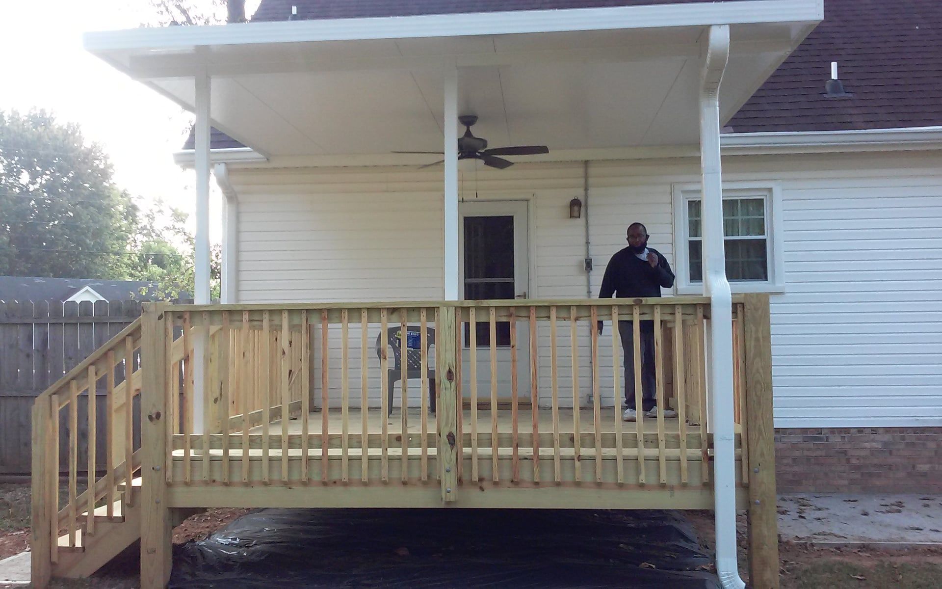 Wooden front porch with railing attached to a white house, with a person standing near the door.