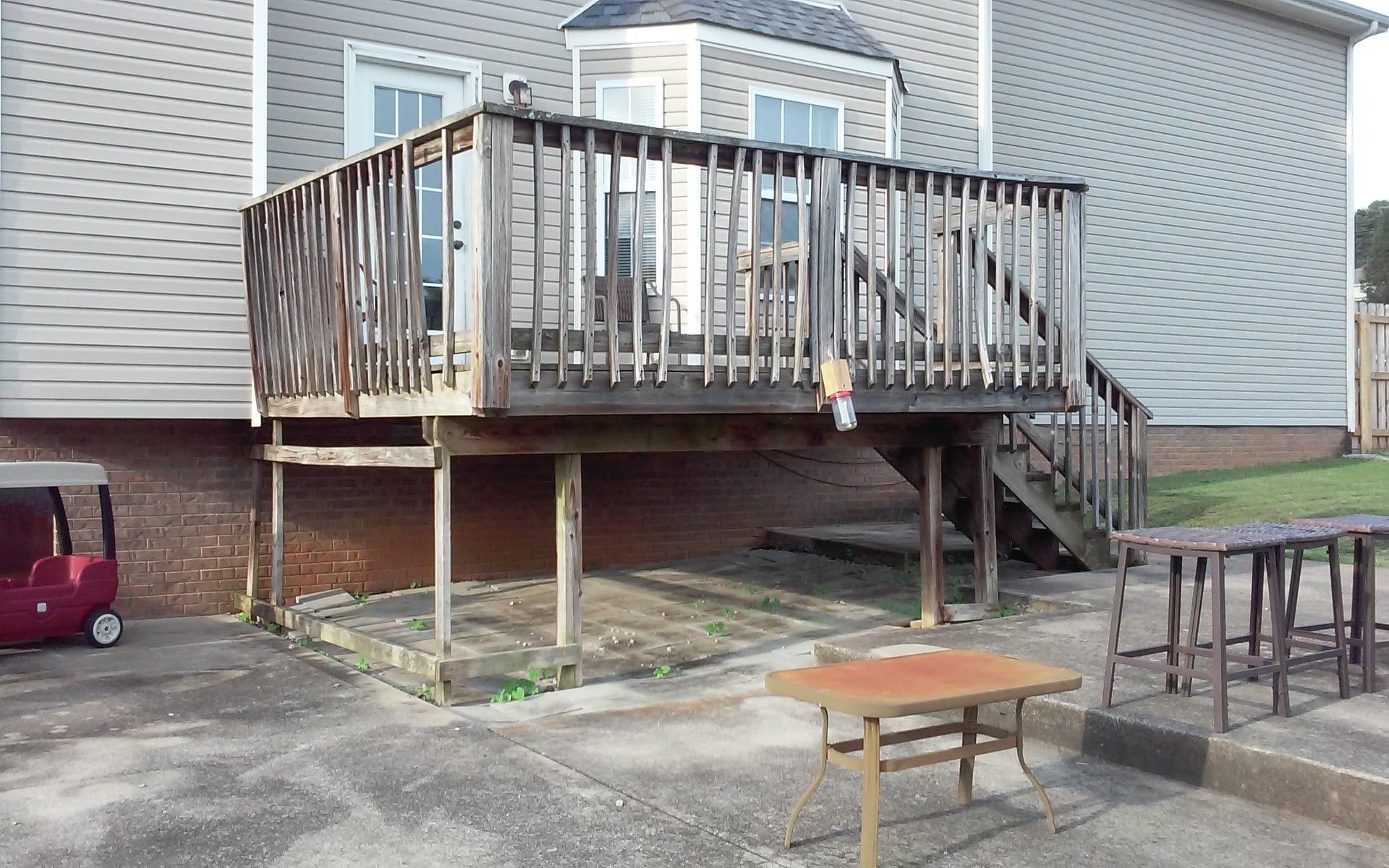 Back deck with wooden stairs and railing over a concrete patio, with small tables and a grill nearby