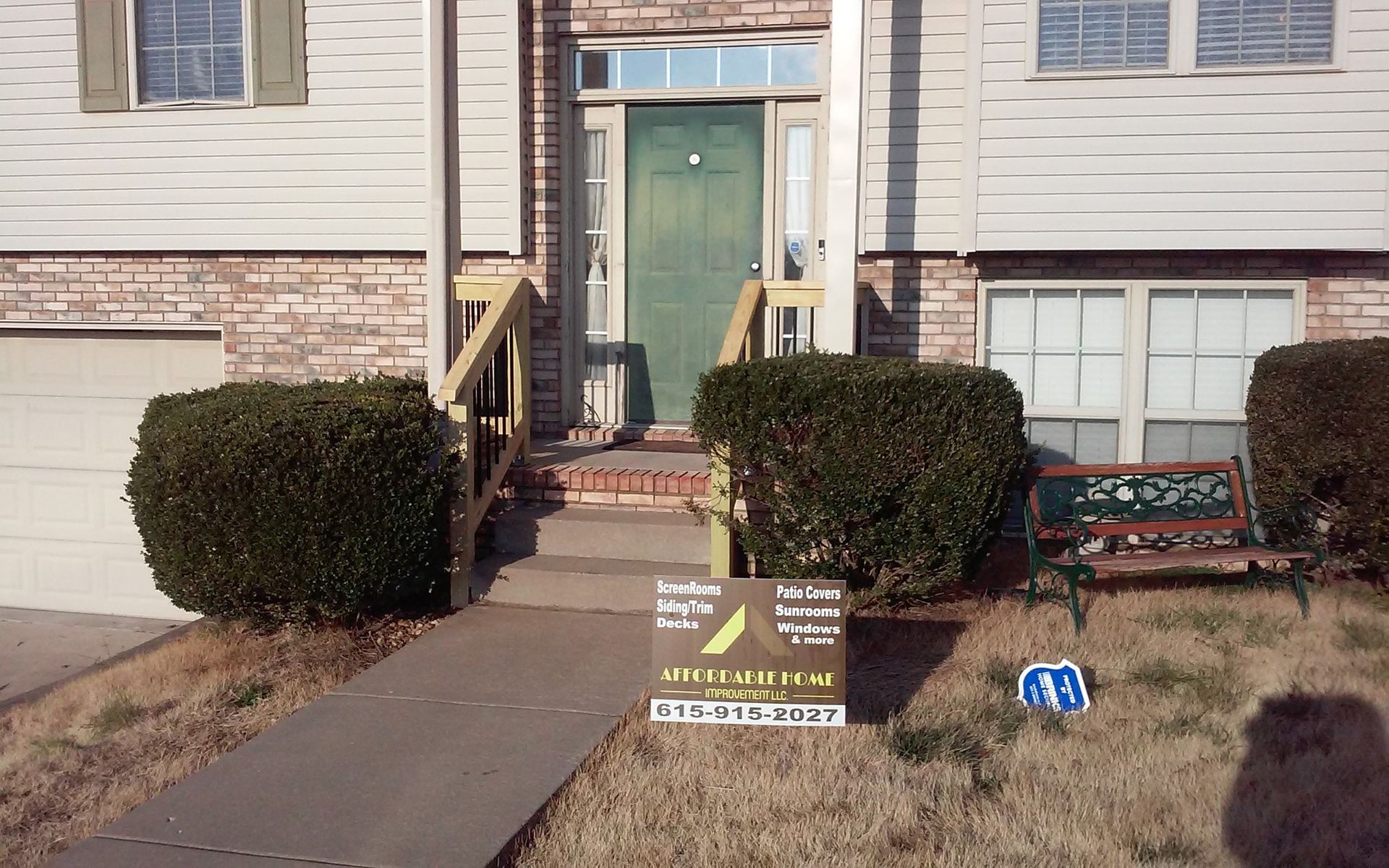 Apartment entrance with two trimmed bushes, a sidewalk, and a small yard sign in front.