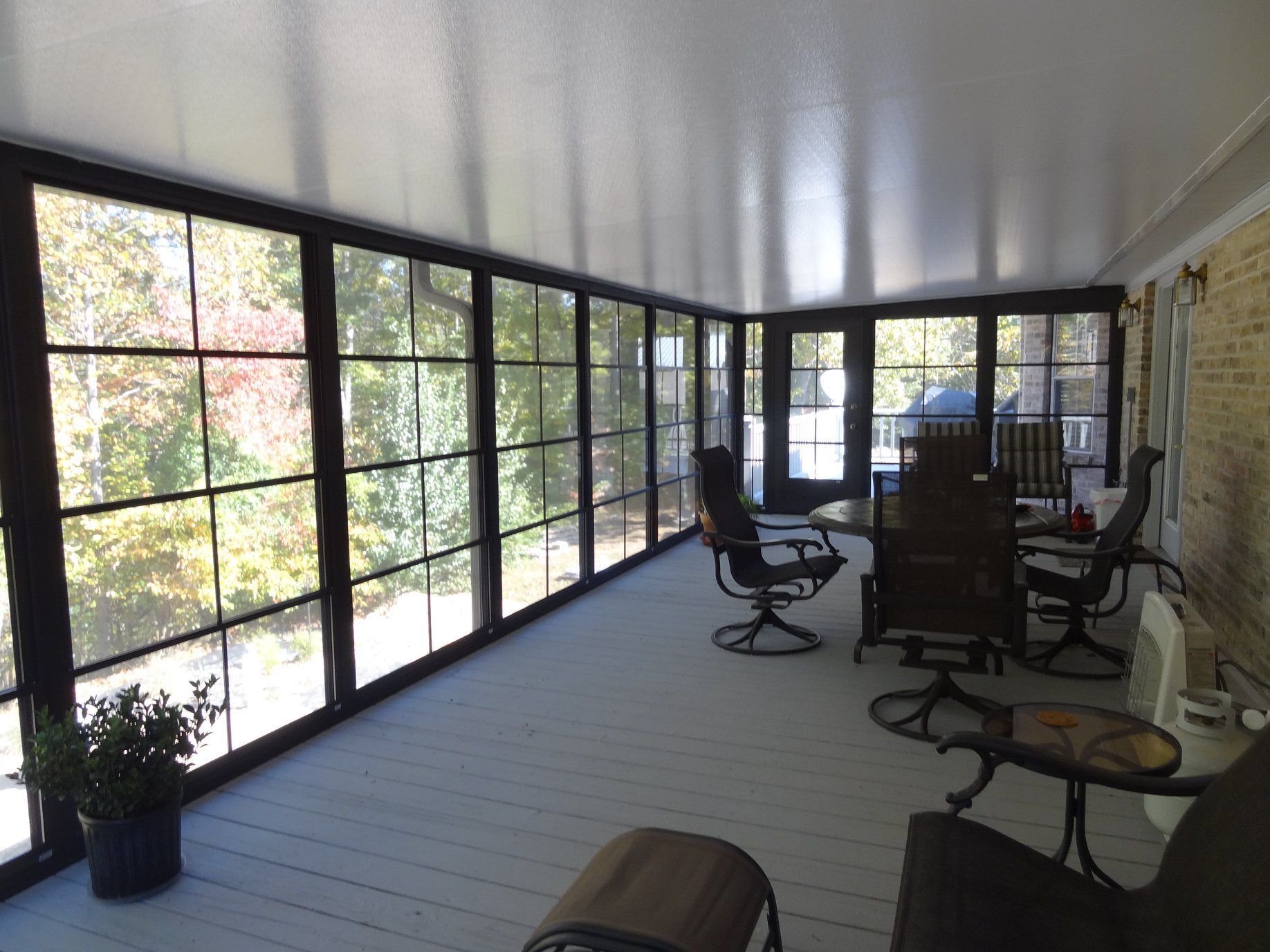 Enclosed sunroom with large windows, gray floor, and patio chairs around a table.