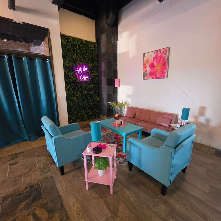 Cozy lounge with teal chairs, pink sofa, colorful decor, and a neon wall sign on a wood floor
