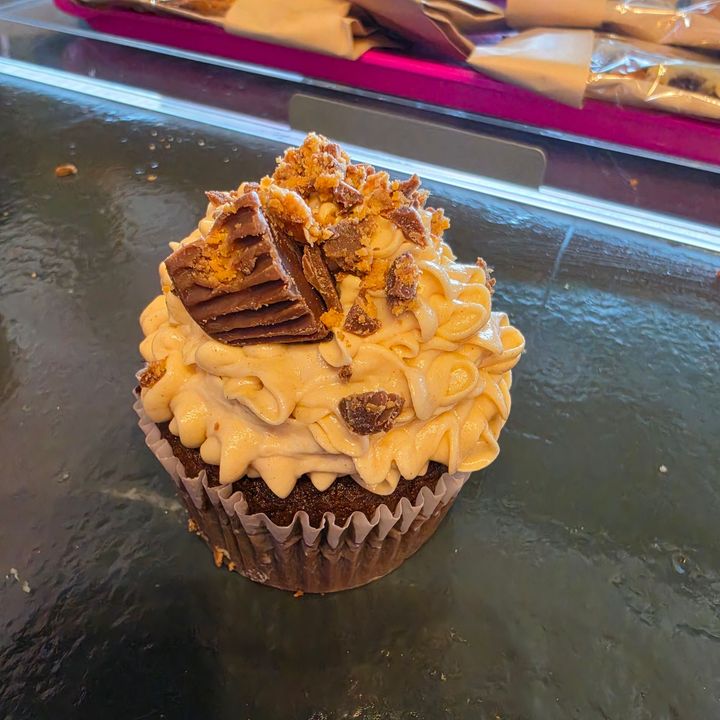 Chocolate cupcake topped with caramel frosting, crumbled candy, and a chocolate piece on a glass table
