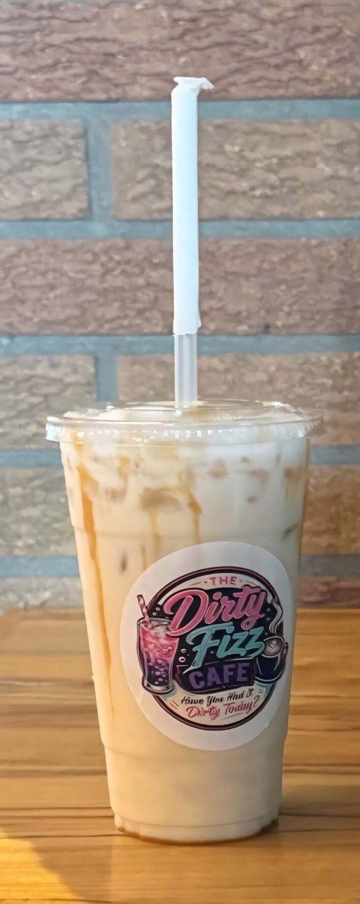 Iced drink in a clear cup with a white straw on a brick wall background