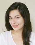 Woman with dark hair smiles, wearing a white shirt against a light background.