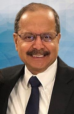 Man with glasses and mustache in a suit smiles.