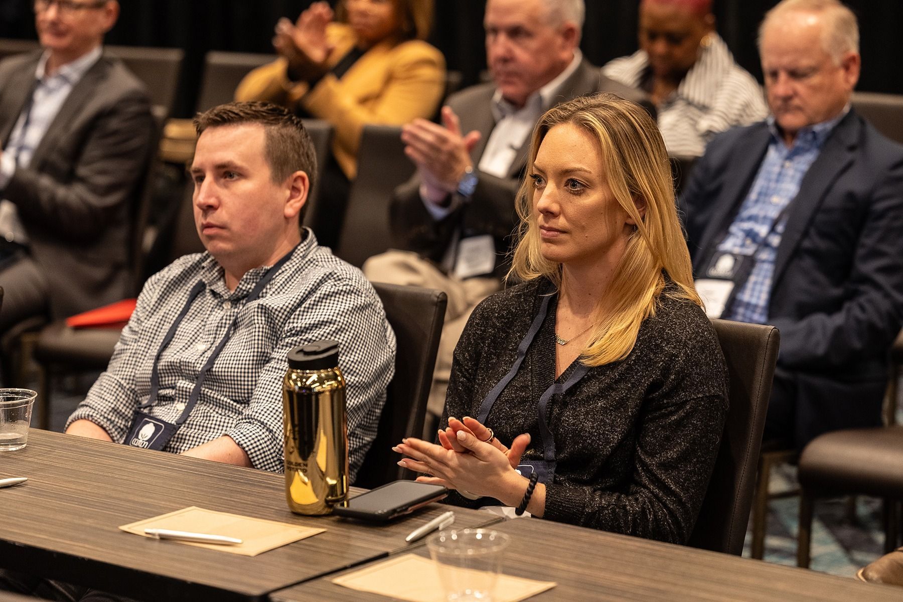 People in business attire at a conference, clapping and listening.