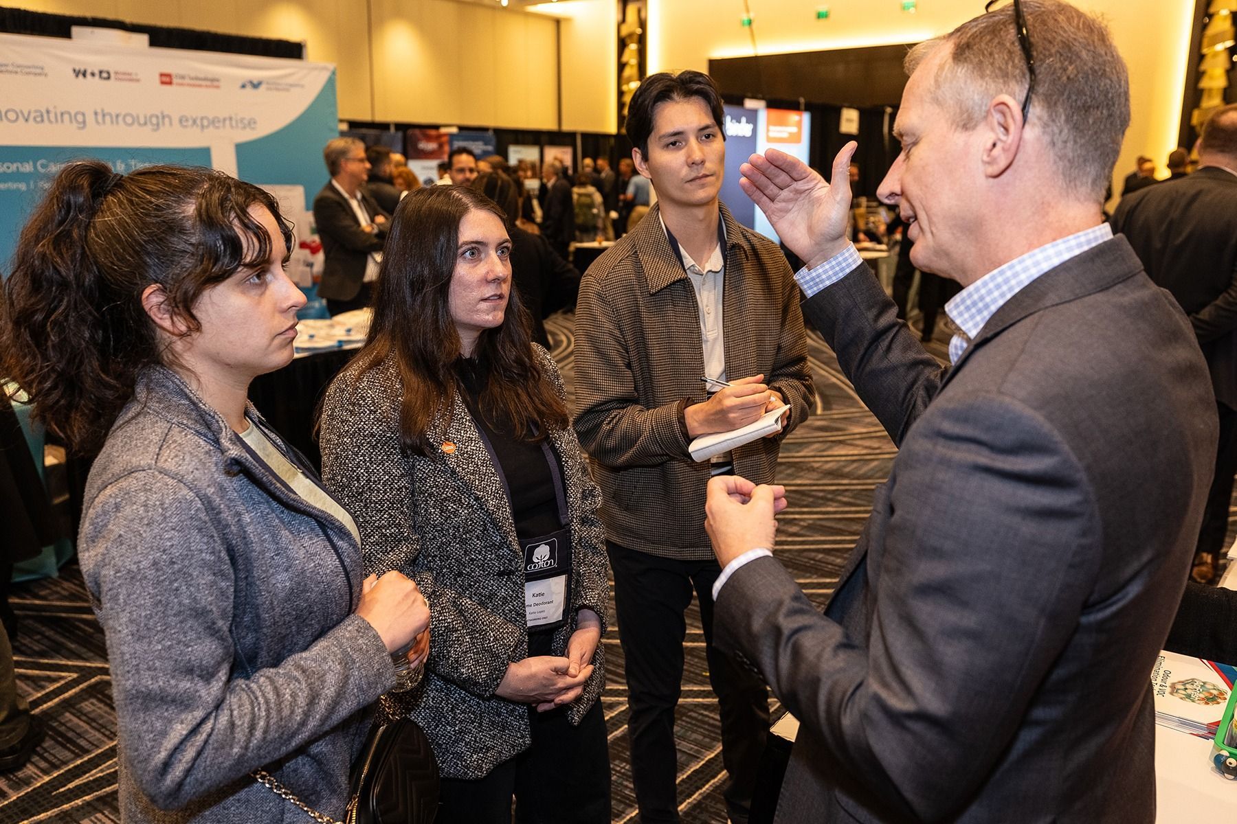 People in business attire engaged in a conversation at a conference, indoors.