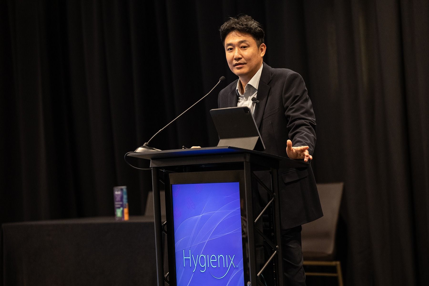 Man speaking at a podium with a screen displaying 