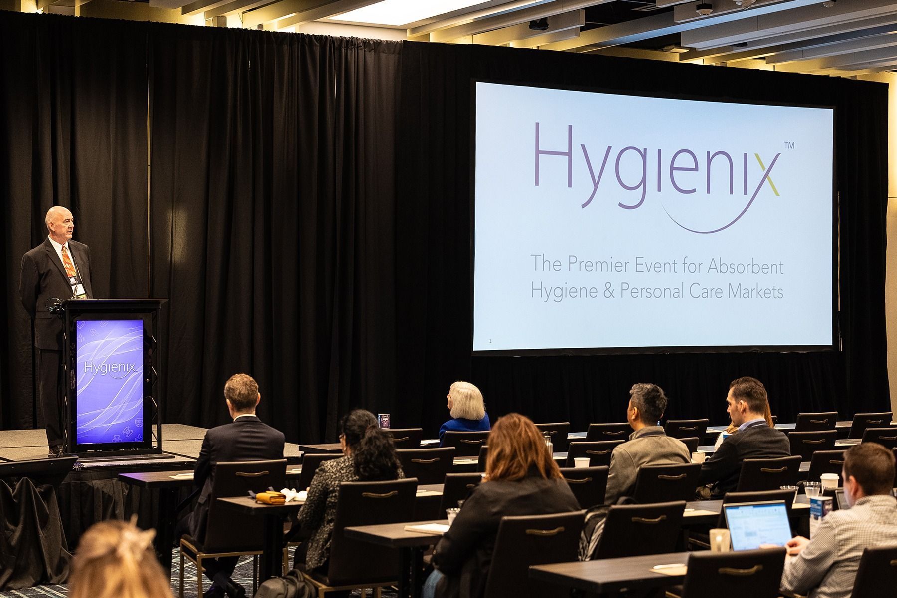 Man speaking at a conference. The screen displays the 