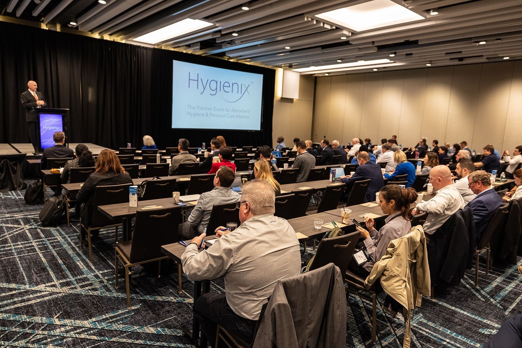 Conference in a large room; a speaker on stage presents to an audience.