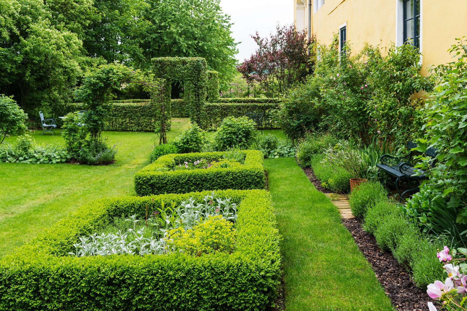 A Lush Green Garden with A Yellow Building in The Background | Clinton, OH | Flexlawn & Landscape, LTD