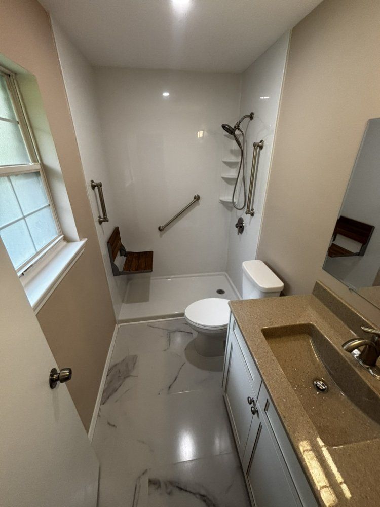 Bright modern bathroom with white toilet, walk-in shower, vanity sink, and grab bars.