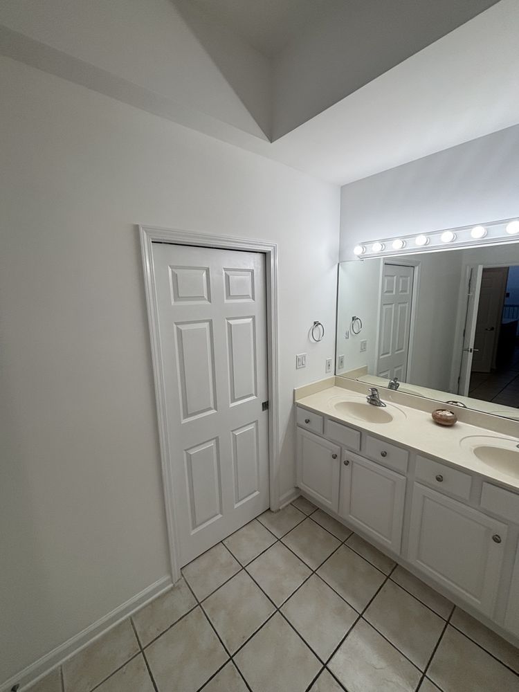 Bathroom with white vanity, large mirror, and closed door; tiled floor and bright lighting.