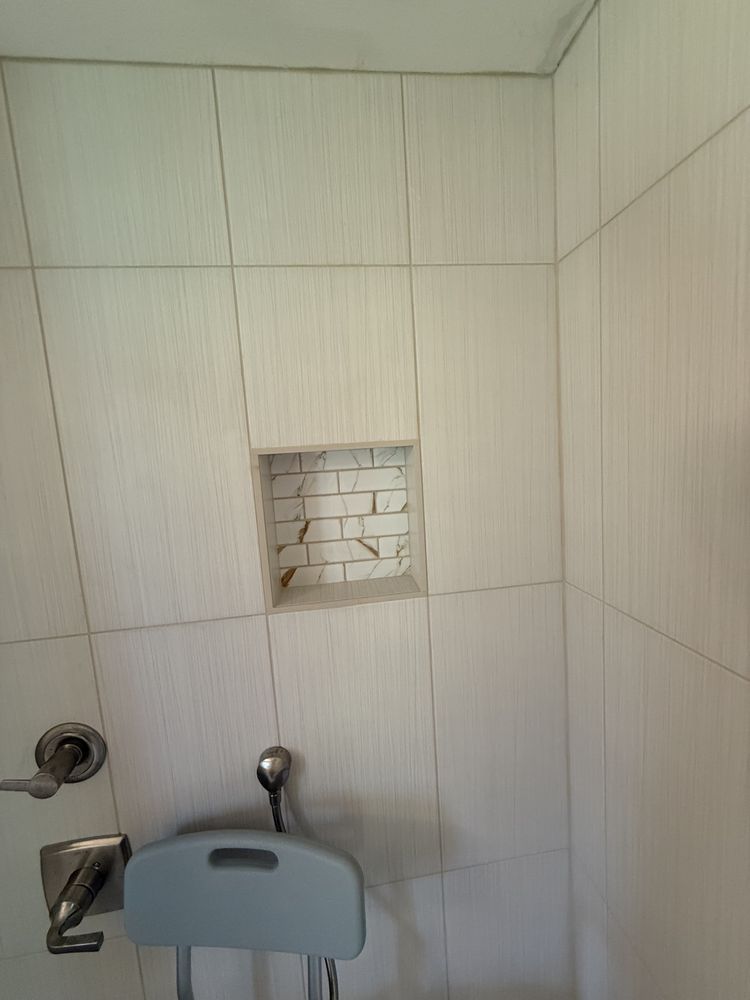 Small tiled bathroom wall with a recessed shelf and a wall-mounted sink faucet below.