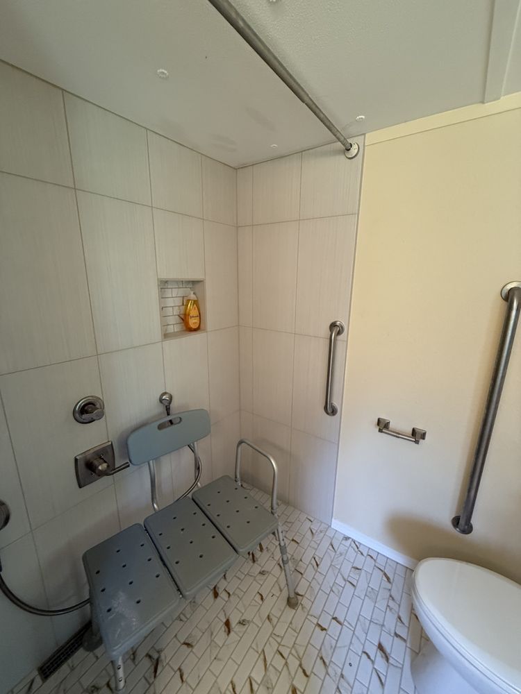Accessible bathroom shower with fold-down seat, grab bars, tiled walls, and toilet beside it