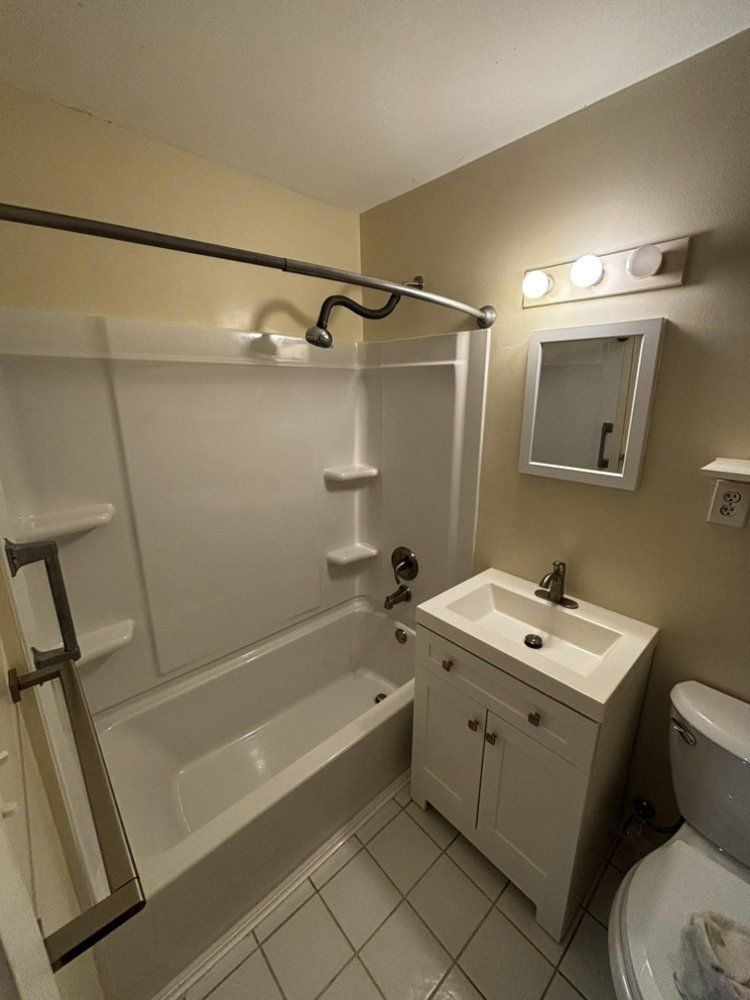 Accessible bathroom with shower-tub, grab bars, sink, mirror, and toilet nearby.