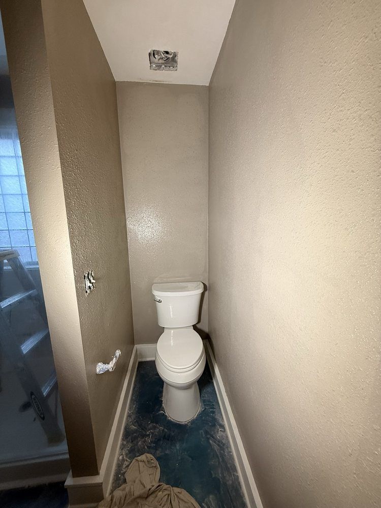 Narrow beige bathroom with a toilet and open door to a shower area.
