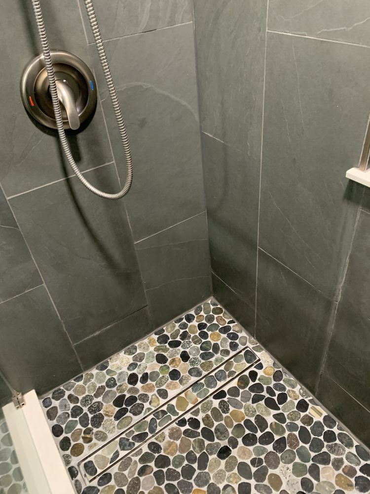 Gray tiled shower with handheld showerhead and pebble-pattern floor drain area