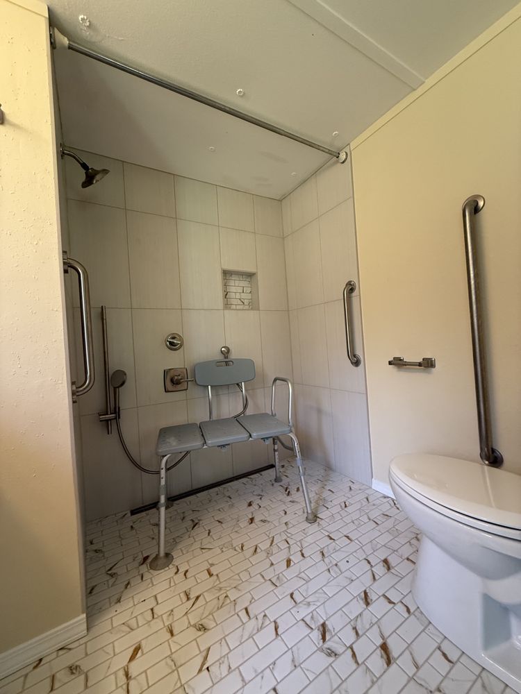 Accessible tiled bathroom with shower bench, grab bars, and toilet; wet floor visible