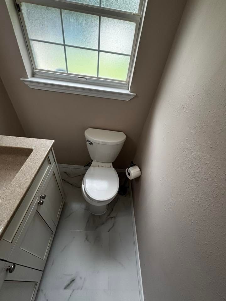 Small bathroom with toilet under a window, gray tile floor, and vanity sink on the left.