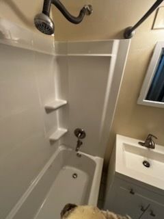 Small bathroom with a shower-tub, built-in shelves, and vanity beside a mirror.