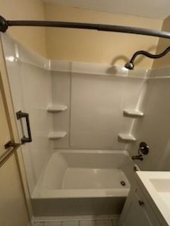 Small bathroom with a tub, shower curtain rod, grab bars, and built-in corner shelves.