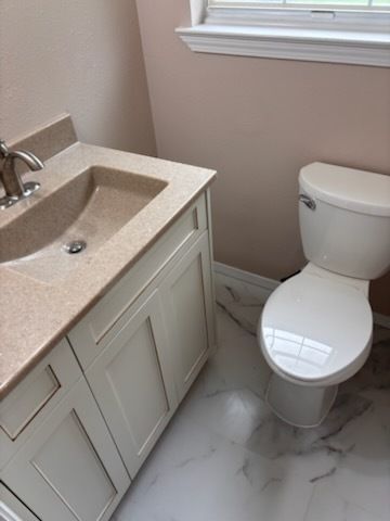 Small beige bathroom with vanity sink, toilet, and window trim on a light marble floor.