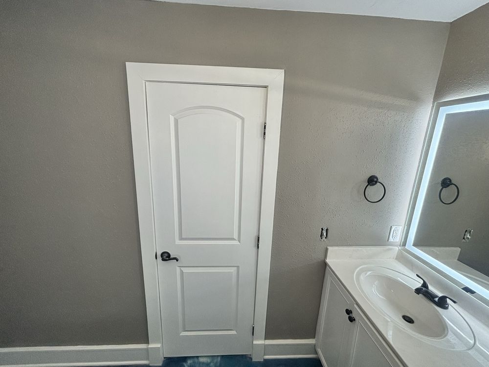 Small bathroom with white door, gray walls, vanity sink, and large mirror.