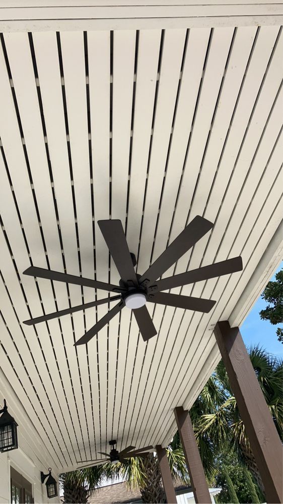 Dark ceiling fan under a white porch roof with columns and trees in the background