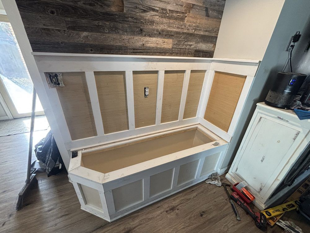 Built-in white bench with gray panels and tan seat against a wall in a room under construction