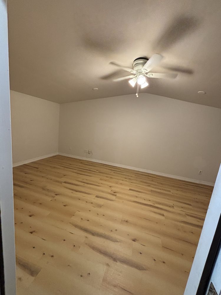 Empty beige room with light wood floor and ceiling fan light on