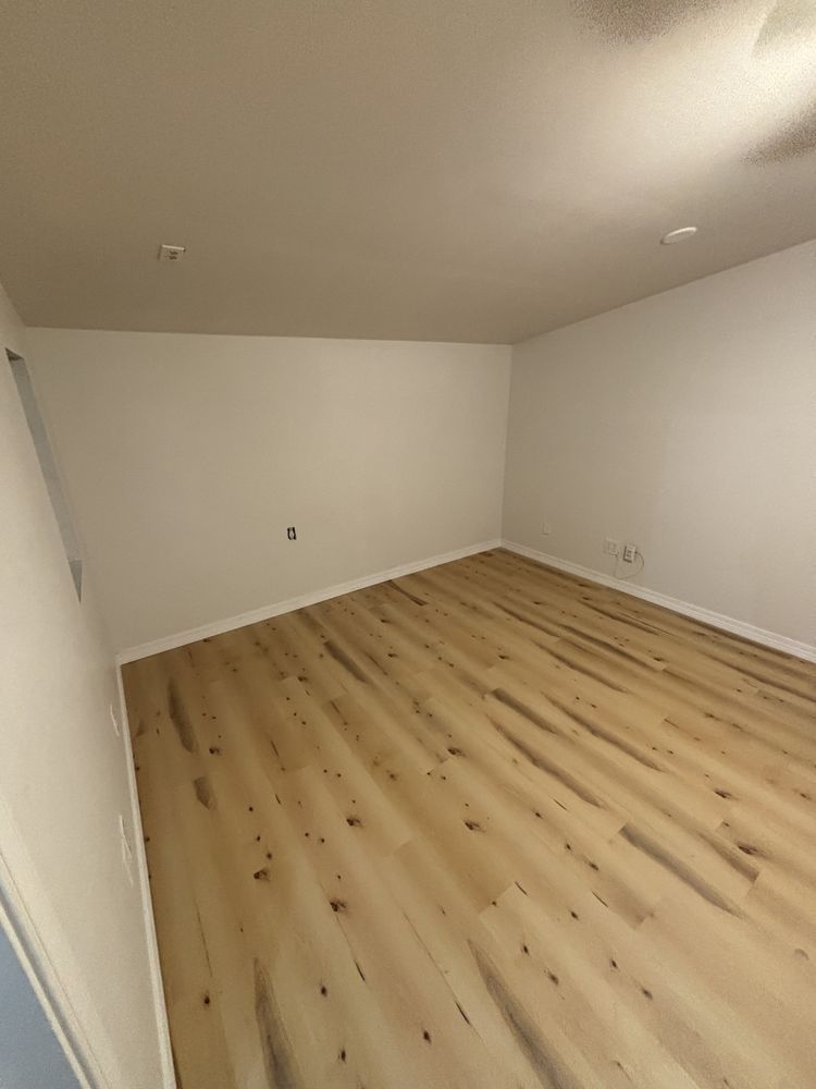 Empty room with light wood flooring, white walls, and a beige ceiling.